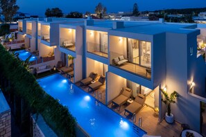 A modern multi-story building with a rooftop pool, outdoor seating, and well-lit balconies. - Oasis Luxury Suites (Rhodes)