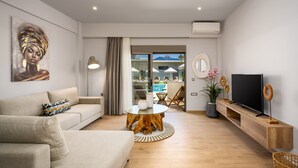 A modern living room with a sofa, a round wooden coffee table, a TV on a wooden stand, and a view of an outdoor pool area.