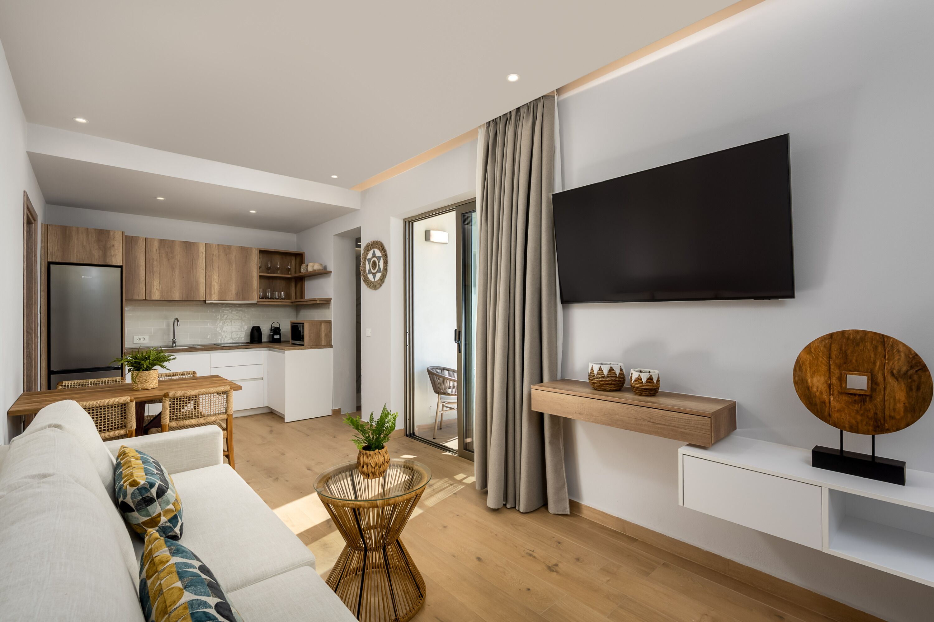 Een moderne woonkamer met een bank, salontafel, tv aan de muur en een keuken in de achtergrond.