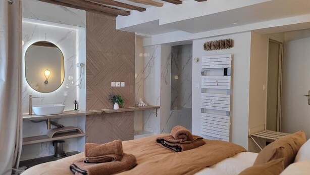 A modern hotel room with a large bed, a round mirror, a built-in sink, and a towel rack. - Tresors de Sens  (Sens)