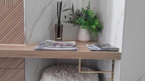 A bathroom with a marble wall, a wooden shelf with magazines, a black reed diffuser, and a potted plant. - Tresors de Sens  (Sens)