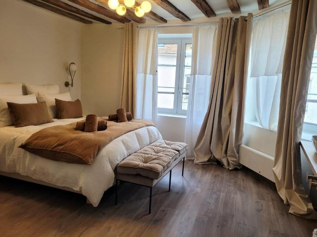 A bedroom with a large bed, a bench, a bedside table, and a window with curtains.