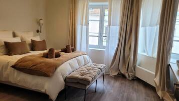 A bedroom with a large bed, a bench, a bedside table, and a window with curtains.