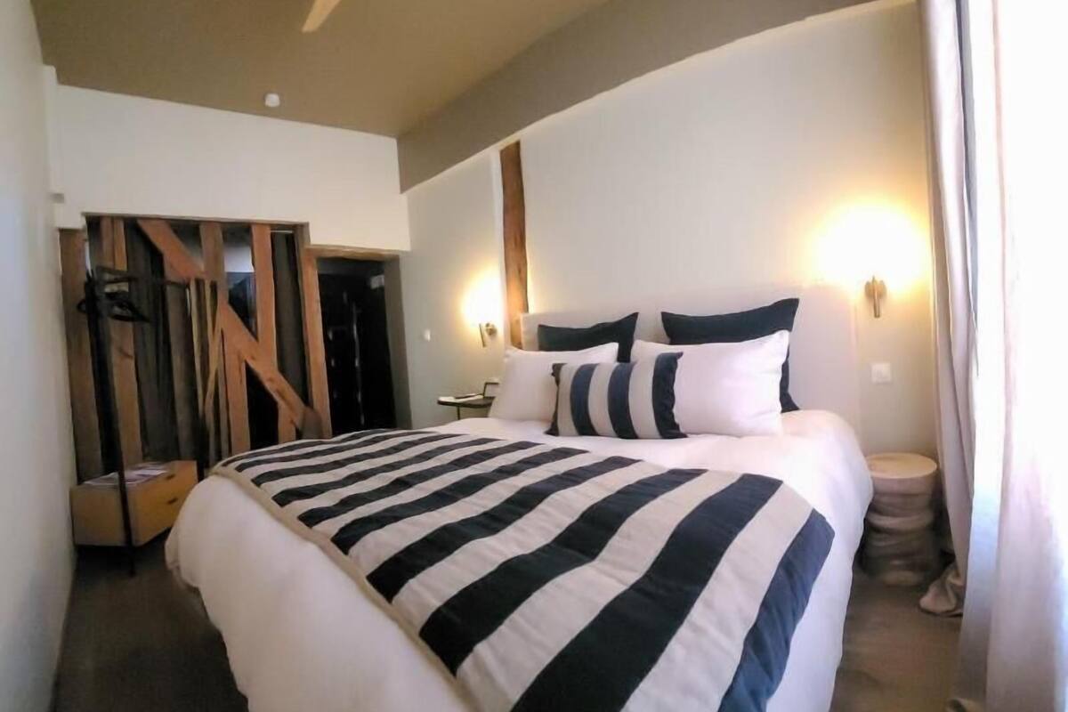 A hotel room with a large bed, a ceiling fan, and a wall-mounted light fixture.