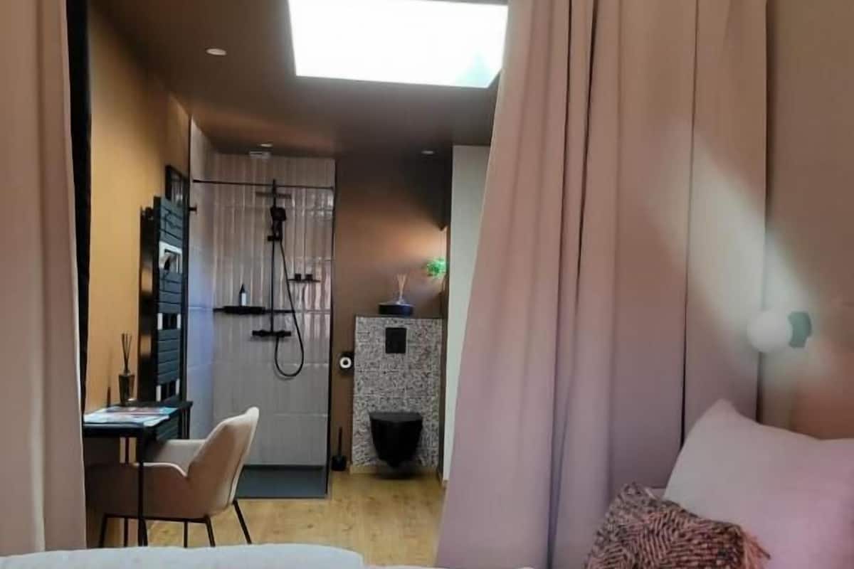 A bedroom with a bed, a desk, and a shower area.