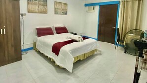 Habitación de hotel con cama, escritorio, silla, ventilador de pie y una puerta.