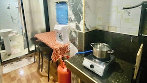 Una cocina compacta con estufa a gas, dispensador de agua y una mesa con mantel rojo.
