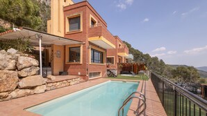 Une villa moderne dotée d’une piscine, d’un mur en pierre et d’un balcon offrant une vue sur un paysage pittoresque.