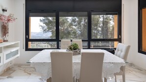 Un coin repas avec une table dressée pour quatre personnes, de grandes fenêtres et une vue sur les arbres et les montagnes.