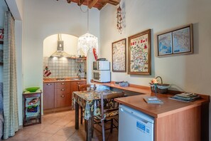 Eine kompakte Küche mit Essbereich, einer Mikrowelle, einem Kühlschrank und einem Spülbecken. An der Wand befinden sich gerahmte Karten, und eine Pendelleuchte ist angebracht.