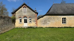 A two-story stone building with a sloped roof, a stone wall on the left, and a grassy lawn in front. - Maison Indépendante (Vallon-sur-Gée)