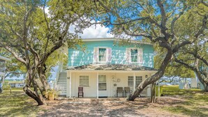 A two-story building with a white exterior and teal shutters, surrounded by trees. - Register - A cozy 2-Bedroom Duplex with Soundfront Views for 6 Guests (Surf City)