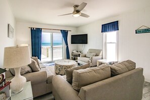 A living room with a sofa, armchair, ottoman, and a flat-screen TV mounted on the wall. - Rest Ashored: Oceanfront 3-bedroom perfect for families (Surf City)