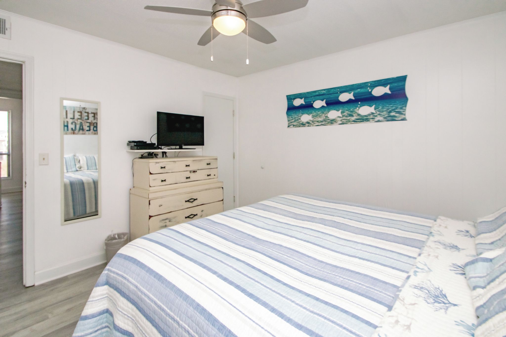 A bedroom with a bed, a dresser, a television, and a ceiling fan.
