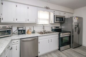 A modern kitchen with white cabinets, a built-in microwave, a stainless steel refrigerator, a dishwasher, and a coffee maker. - Rest Ashored: Oceanfront 3-bedroom perfect for families (Surf City)