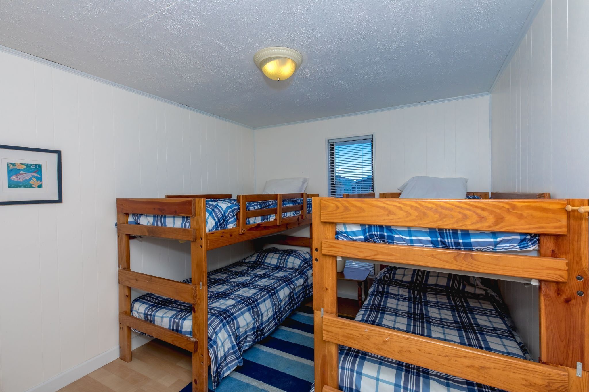 A dormitory room with bunk beds, a framed picture on the wall, and a ceiling light.