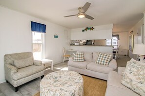 A living room with a sofa, armchair, and ottoman, a ceiling fan, and a view into the kitchen. - Rest Ashored: Oceanfront 3-bedroom perfect for families (Surf City)