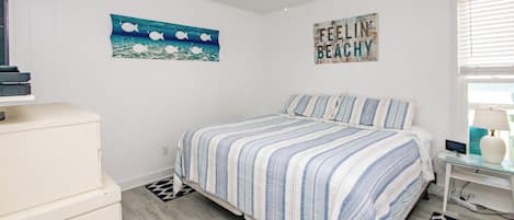 A bedroom with a bed, a ceiling fan, a wall with a 'FEELIN' sign, and a window with blinds.