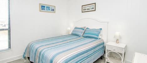 A bedroom with a bed, a nightstand, a lamp, a chair, and two framed pictures on the wall.