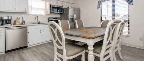 A modern kitchen with white cabinets, stainless steel appliances, and a dining area with a wooden table and upholstered chairs.