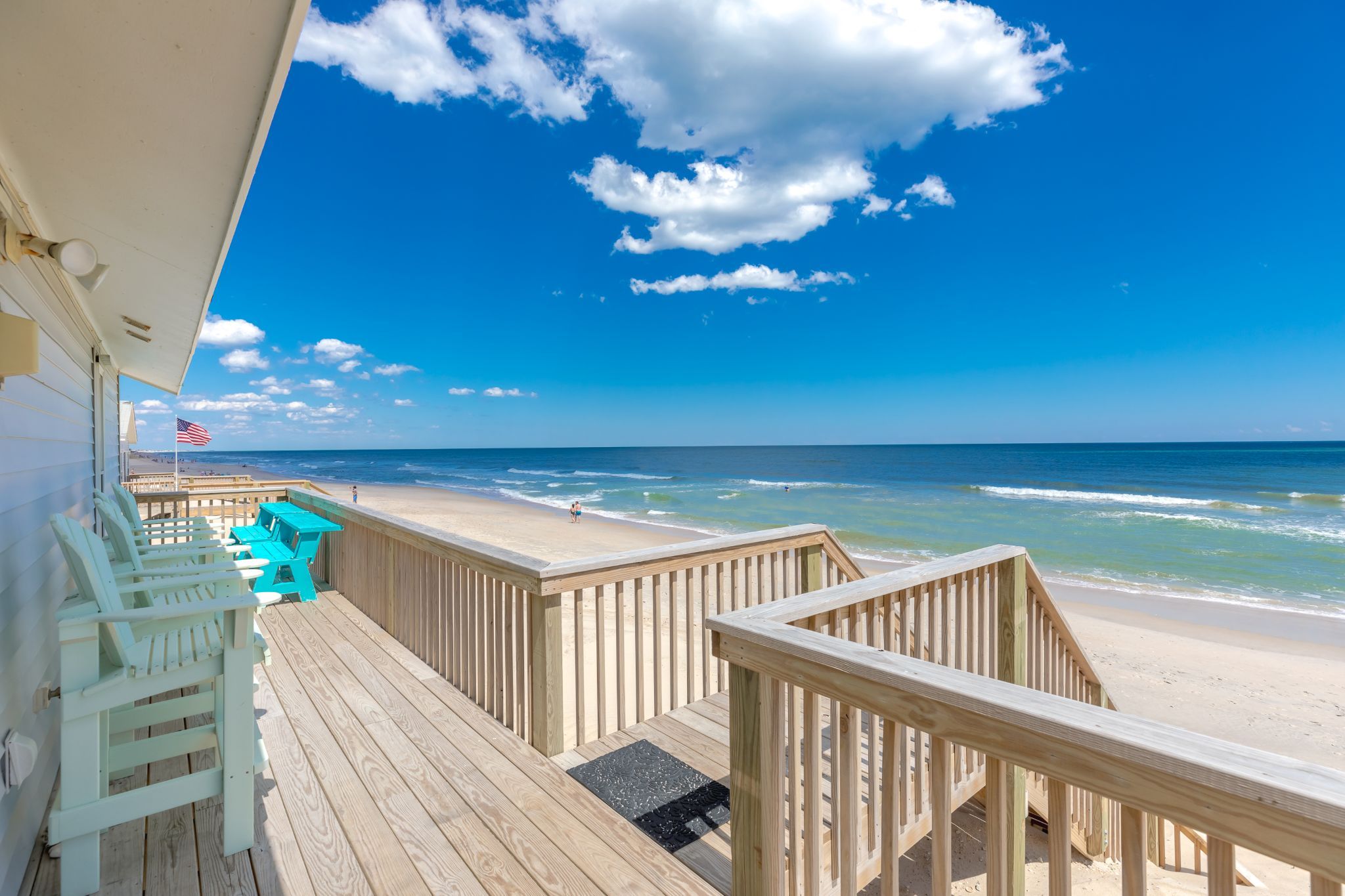 A wooden deck with a view of the beach and ocean.