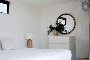 A bedroom with a bed, a lamp, a mirror, a dresser, and a fan.