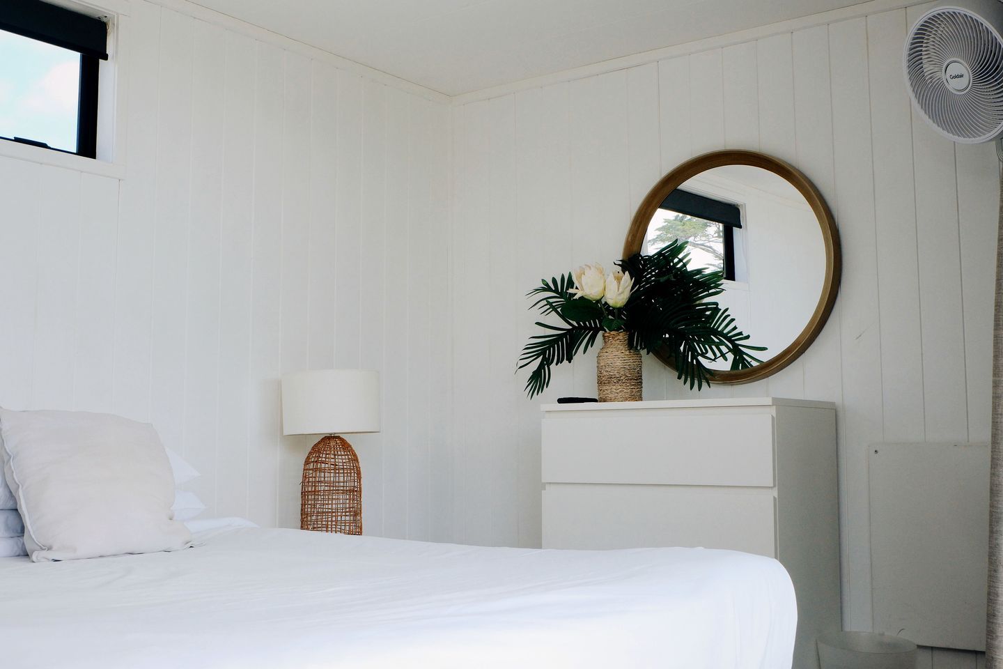 A bedroom with a bed, a lamp, a mirror, a dresser, and a fan.