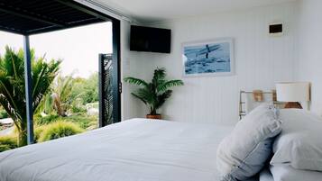 Une chambre à coucher avec un lit, un téléviseur fixé au mur, une plante en pot et une vue sur la verdure à l’extérieur.