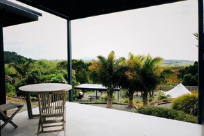 Une terrasse extérieure avec une table ronde et des chaises, entourée d’une végétation luxuriante et offrant une vue sur des collines lointaines.