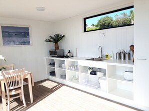 Une cuisine de taille modeste avec des meubles blancs, un coin repas comprenant une table et des chaises en bois, une plante en pot et une vue sur l’extérieur.