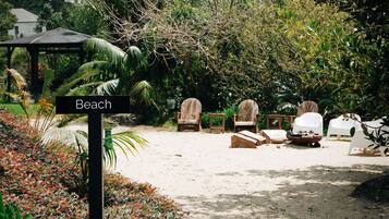 A beach area with a sign labeled 'Beach,' surrounded by various seating options including wooden chairs and white plastic chairs.