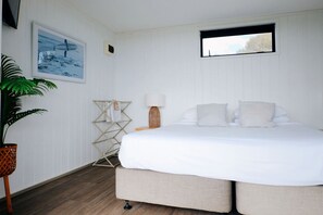 Un dormitorio con cama, ventana, lámpara de pared, tendedero y un cuadro enmarcado.