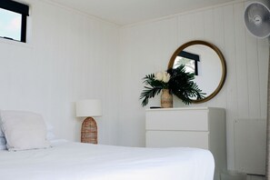 Een slaapkamer met een bed, een lamp, een spiegel, een dressoir en een ventilator.