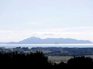 Paisaje costero con montañas, una masa de agua y un barco a lo lejos.
