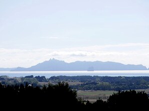 Paisaje costero con montañas, una masa de agua y un barco a lo lejos.