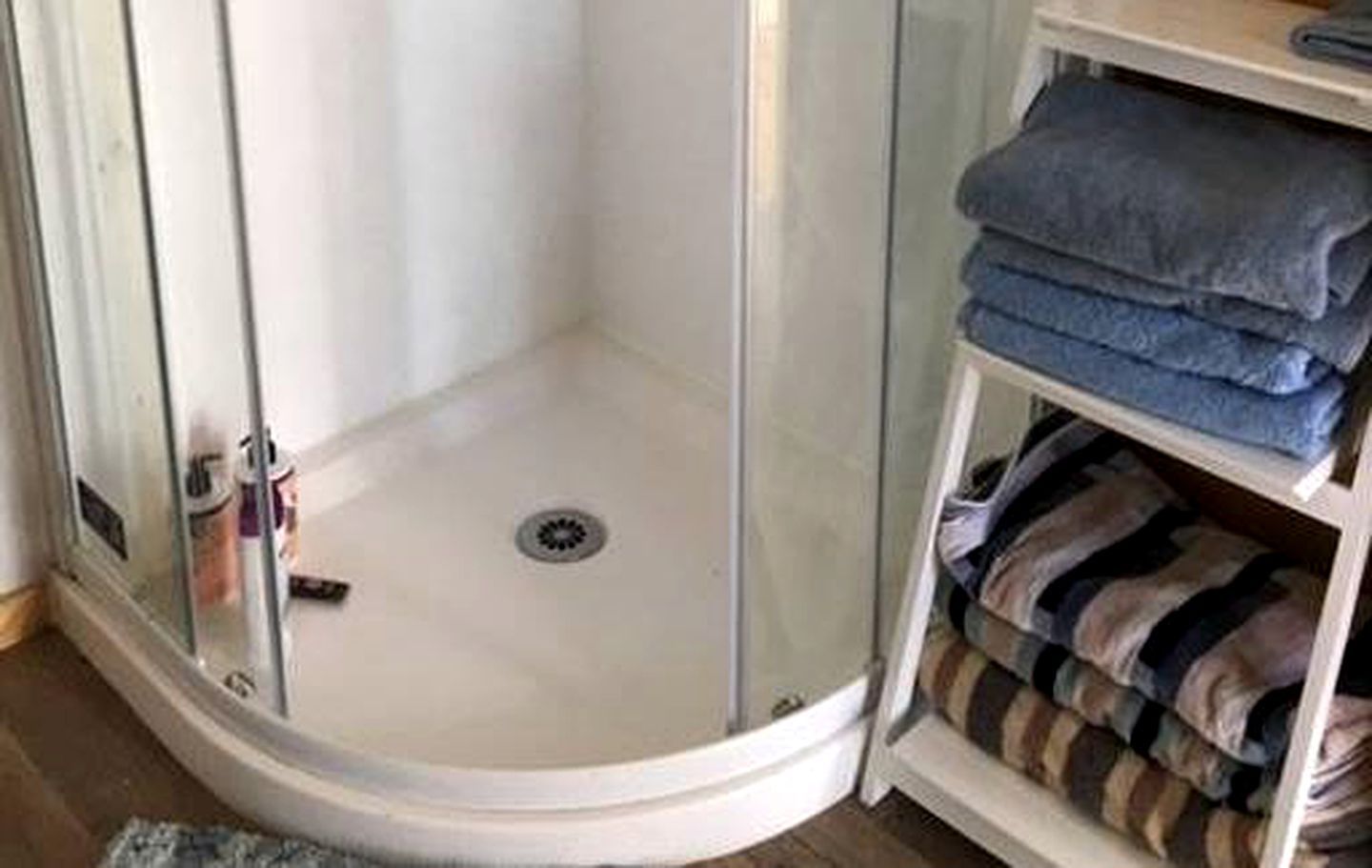 A shower with a glass door, a white sink, and a towel rack with folded towels.