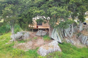 Une terrasse en bois dotée d’un espace salon intégré, entourée de gros rochers et d’arbres.