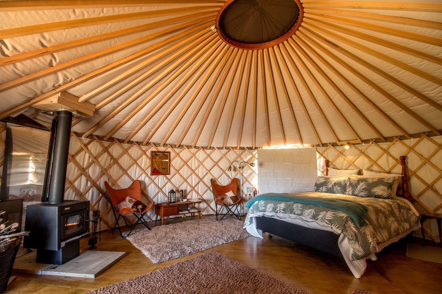 A yurt with a bed, a small table, chairs, a heater, and a window.
