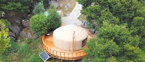 Una estructura de domo geodésico con cubierta de madera, rodeada de abundante follaje y rocas.