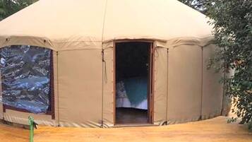 A large, beige tent with an open entrance, a wooden deck, and a large window on one side.