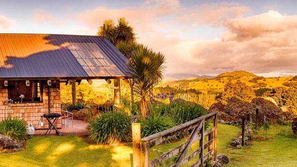 A rustic building with a metal roof, surrounded by lush greenery and a wooden fence.