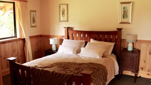 A wooden four-poster bed with a brown bedspread, two bedside tables with lamps, and framed pictures on the walls.