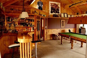 A bar area with wooden walls, a pool table, and a billiards table.