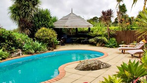 A swimming pool with a curved edge, surrounded by various plants and a gazebo.