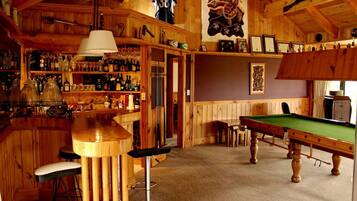 A bar area with wooden walls, a pool table, and a billiards table.
