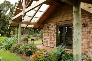 Edificio de madera con fachada de ladrillo, puerta de vidrio y un patio cubierto con plantas y una parrilla.
