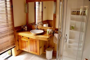A bathroom with wooden cabinetry, a white sink, a mirror, and a shower enclosure.