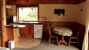 A compact kitchen with wooden cabinets, a refrigerator, a sink, and a dining area with a table and chairs.