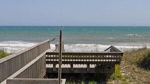 Ein hölzerner Steg führt zu einem Strand, wo Wellen auf die Küste branden.