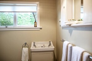 A bathroom with a window, a sink, a towel rack, and a shelf with toiletries.